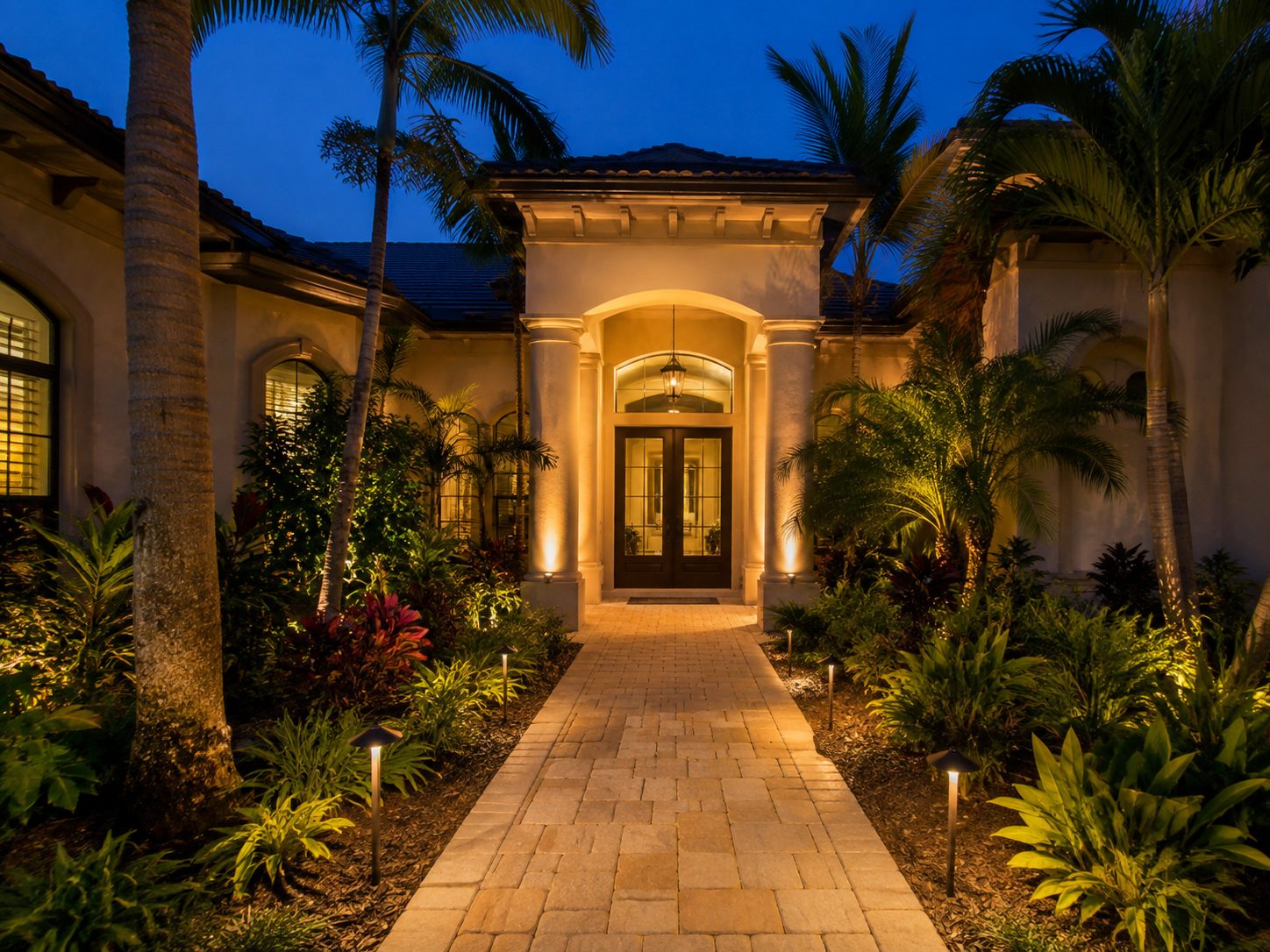 Warm landscape lighting on the columned front entry and paver walkway of a Tampa FL home at night