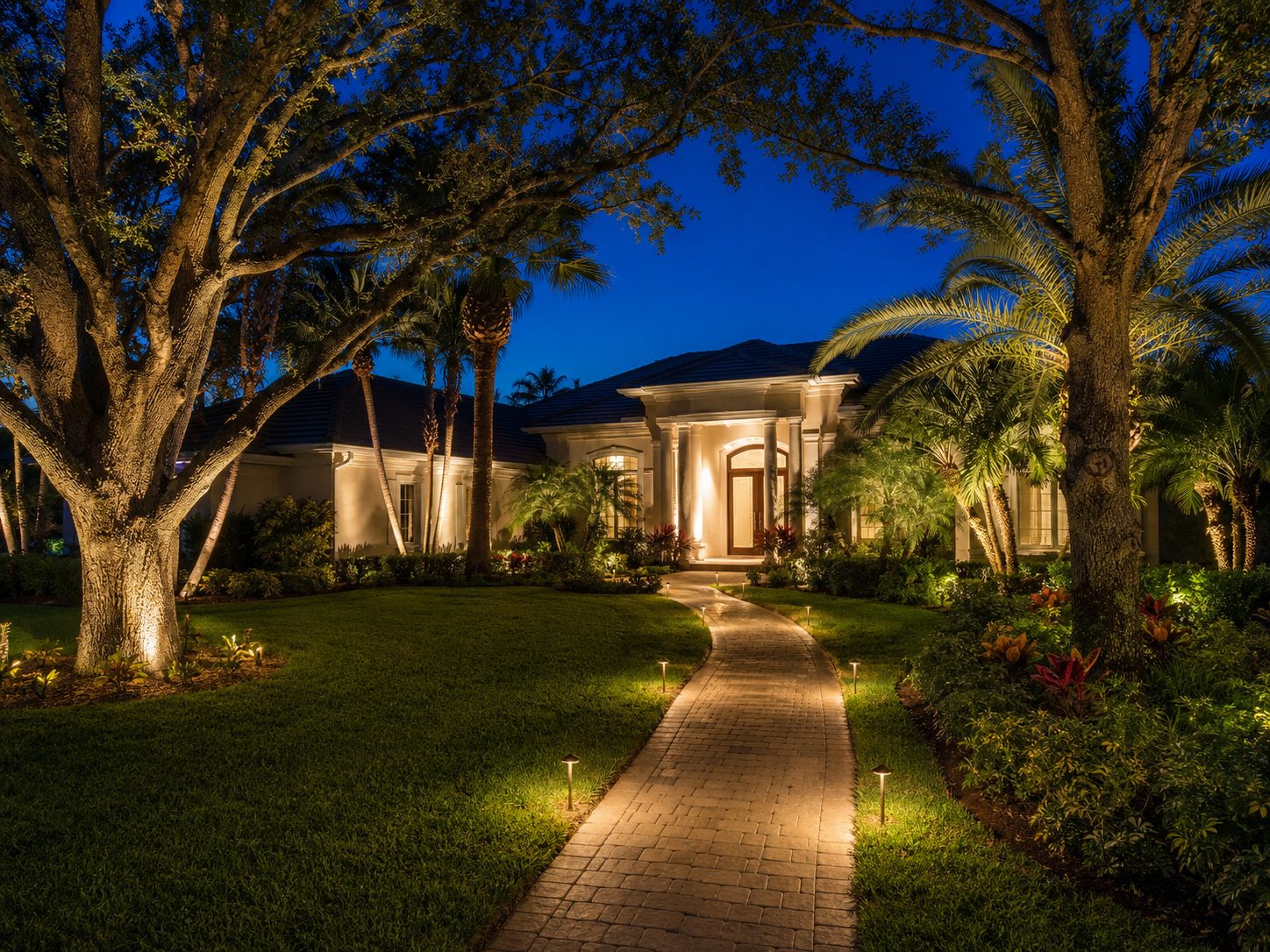 Oak and palm uplighting with a lit pathway across the front yard of a Tampa FL home at dusk